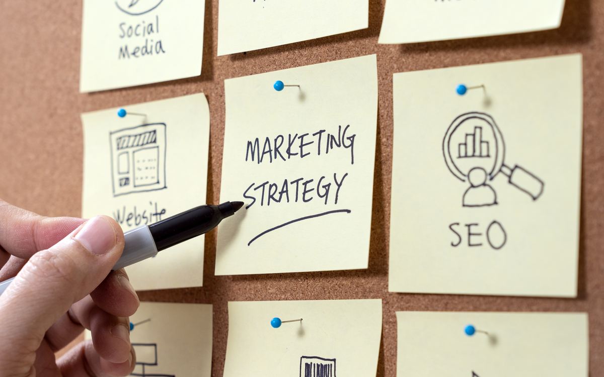 Manos anotando «Marketing Strategy» y «SEO» en notas adhesivas sobre un corcho