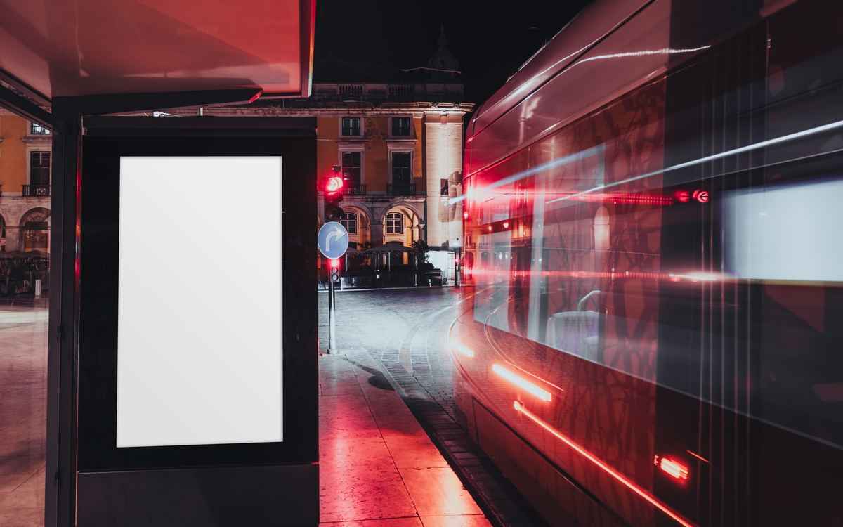 Paradero urbano de noche con un anuncio luminoso en blanco y luces de vehículos en movimiento