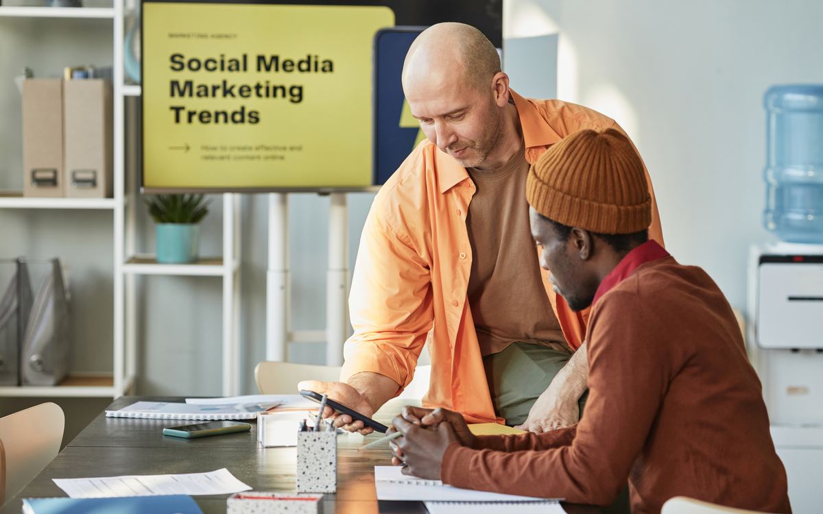 Dos personas revisando contenido en una tablet frente a una pantalla con tendencias de marketing en redes sociales