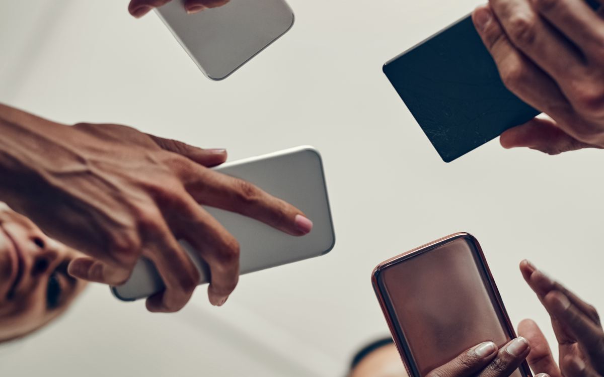 Manos de varias personas sosteniendo teléfonos en círculo, compartiendo contenido en pantalla